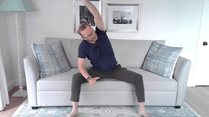 Man leaning to the side with his arm stretched overhead while sitting on the couch