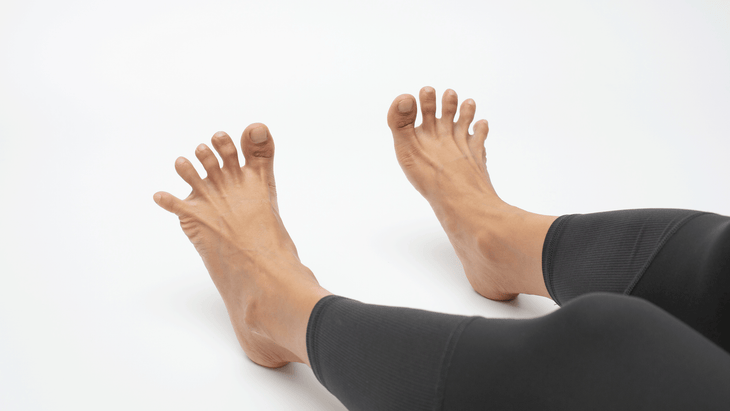 Woman in yoga leggings practicing toe stretches by taking them wide apart.