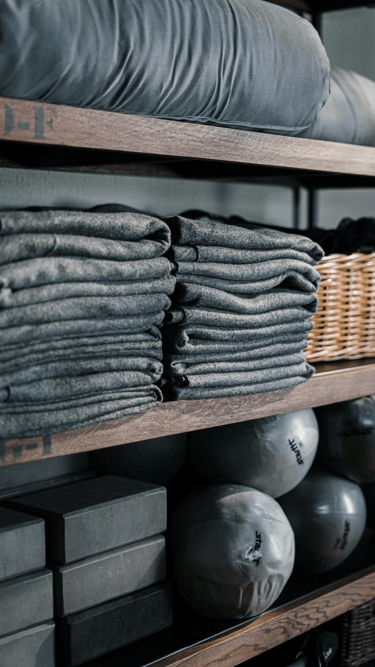 A wall of yoga props, including folded blankets and blocks stacked neatly