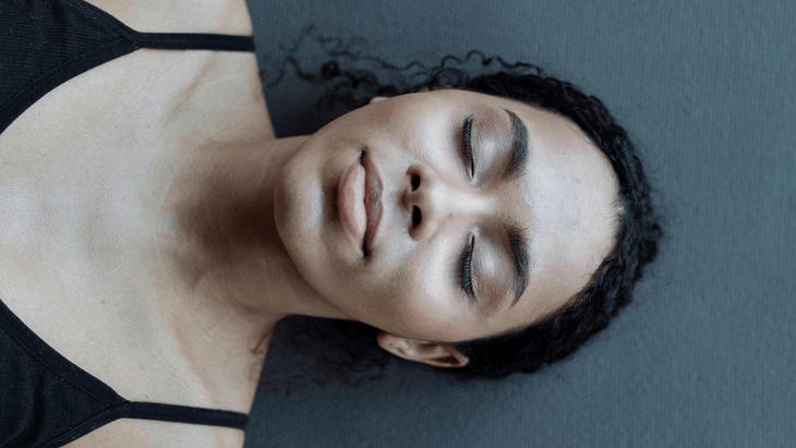 Woman lying on a mat practicing Savasana and good yoga etiquette