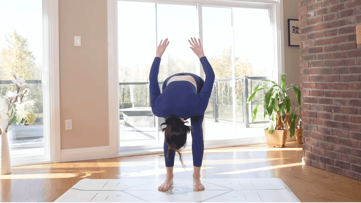 Woman practicing on a yoga mat folding forward and sweeping her arms behind her