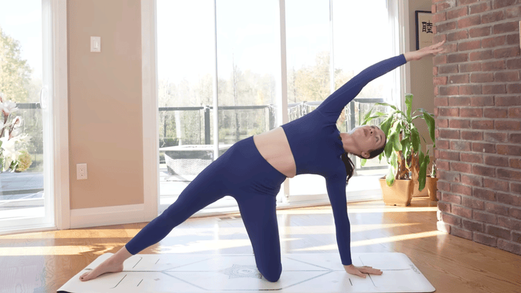 Woman on yoga mat with one hand and knee on the mat in a side stretch