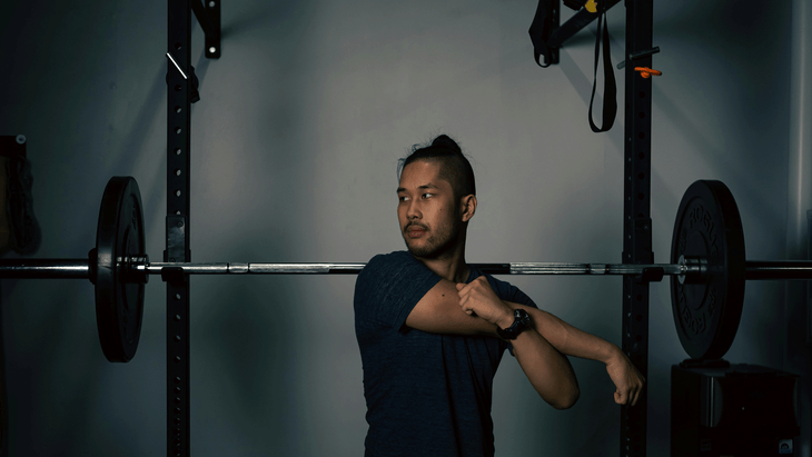 Man at a gym in front of a dumbbell practicing shoulder stretches