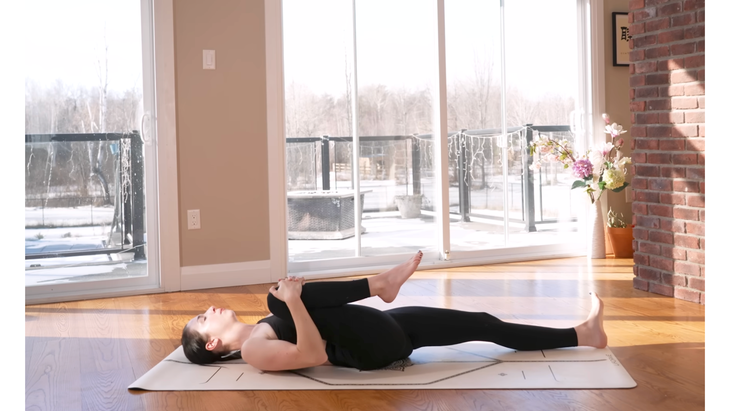 Woman lying down on a yoga mat drawing one knee to her chest in a reclined stretch