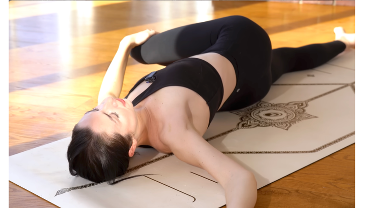 Woman lying on a yoga mat in a reclined twist with her right knee leaning across her body 