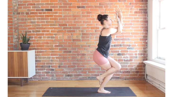 Woman standing at front of mat in Eagle Pose