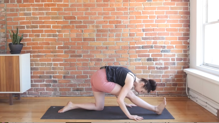 Woman practicing half splits with her front leg straight on a yoga mat