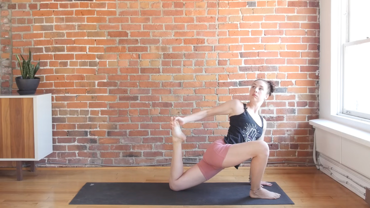 Woman kneeling on a yoga mat and reaching behind for her right foot