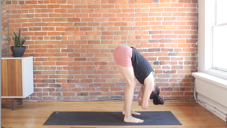 Woman in a standing forward fold at the top of her yoga mat during a minimal cues yoga class