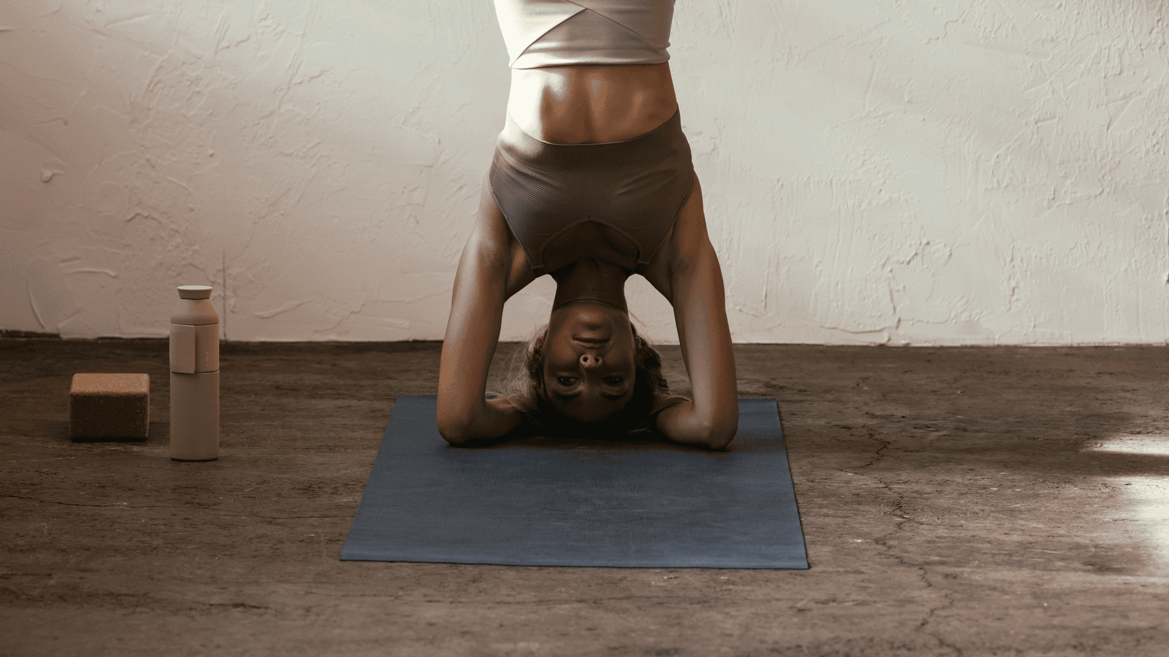 Woman on a yoga mat practicing headstand, one of several yoga poses to avoid, according to some teachers