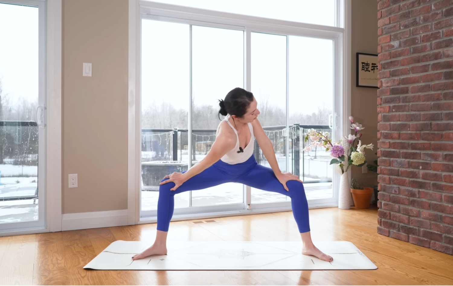 Woman on a yoga mat in Goddess Pose while twisting chest and shoulders to the side