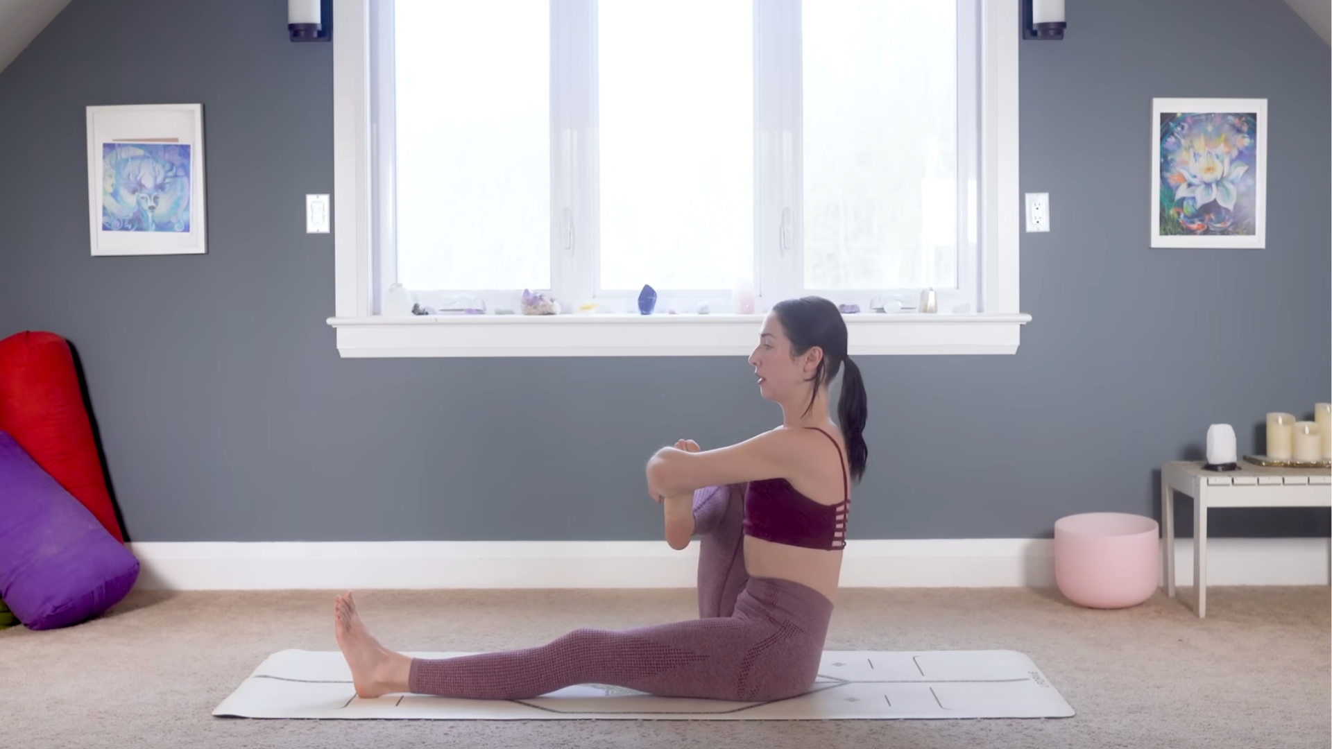 Woman sitting on a yoga mat holding her right shin to her chest in hip opening stretches