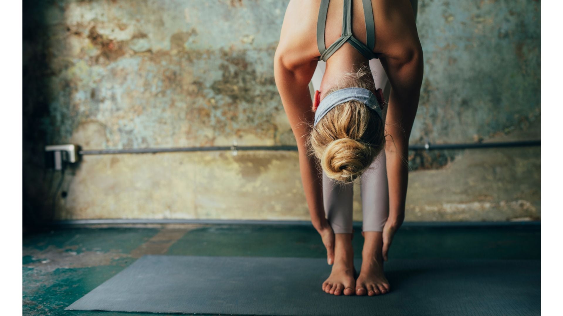 A woman standing in a forward bend on a yoga mat while contemplating causes of shoulder pain