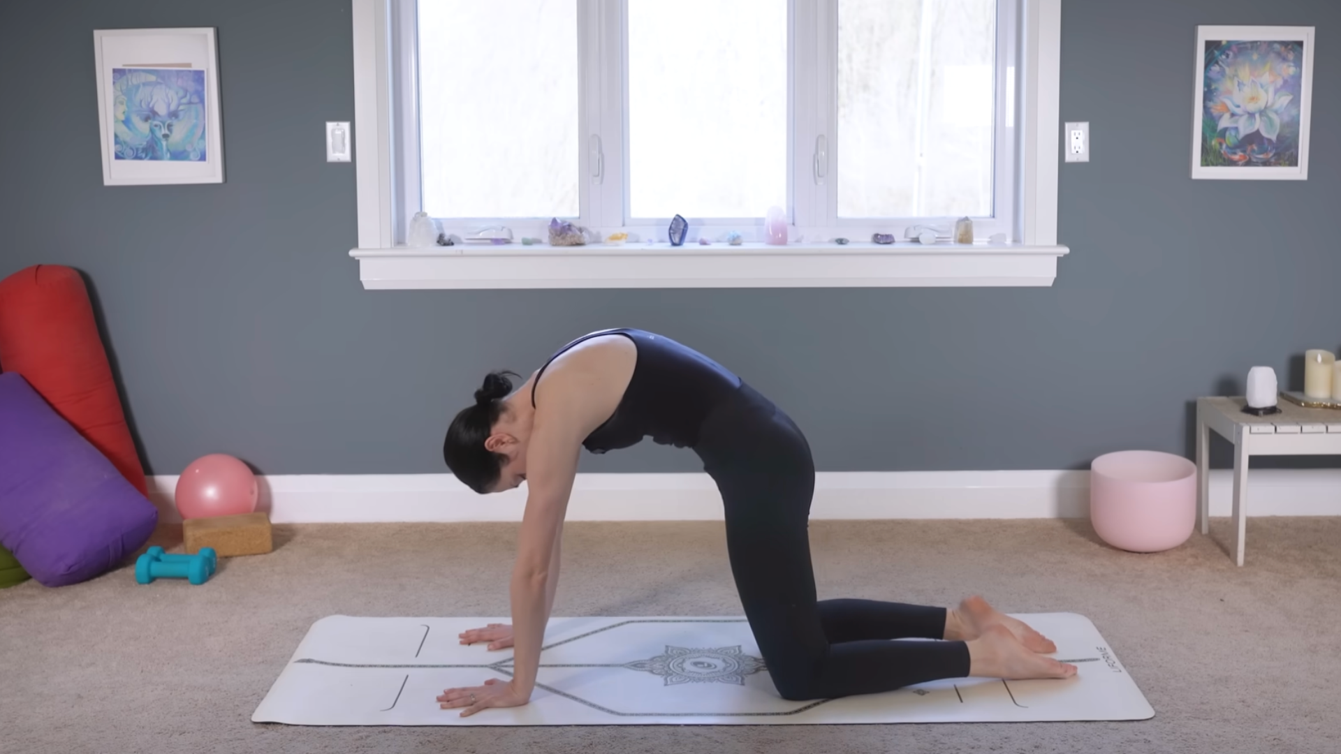 Yoga teacher kneeling on a mat rounding her back in Cat Pose