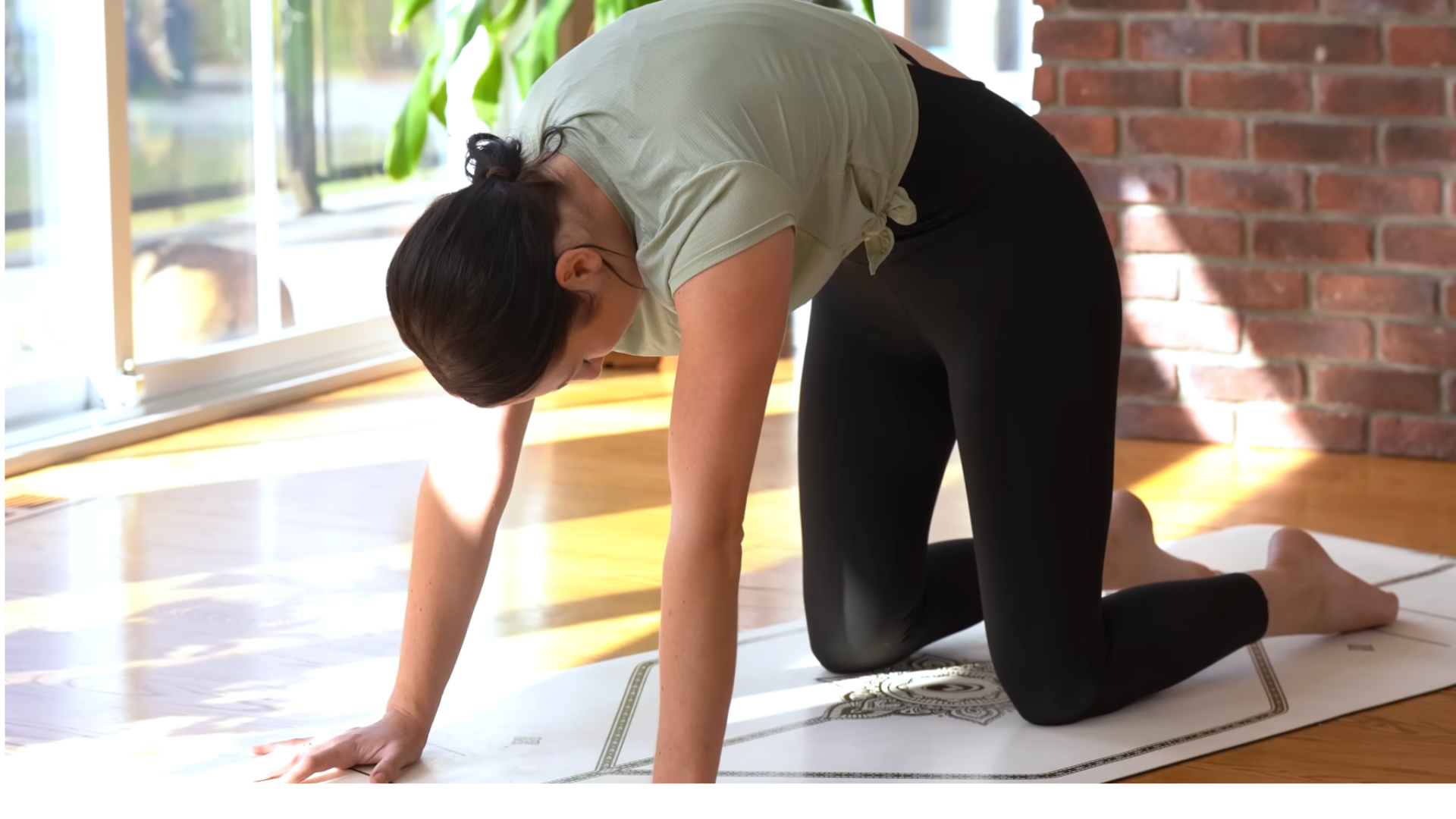 woman kneeling on a yoga mat in Cat Pose with her back rounded