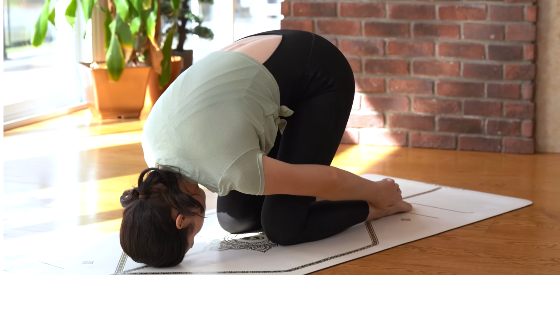 Woman kneeling on a mat with her head on the ground for a back stretch