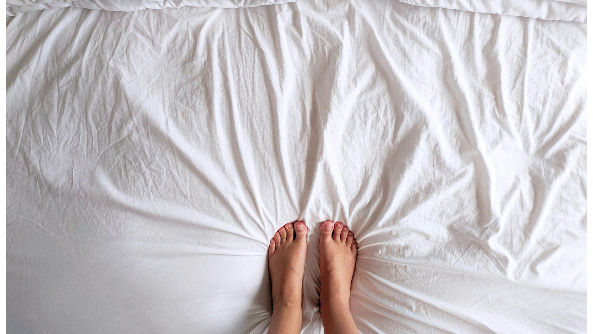 Bare feet resting on white sheets while doing bed yoga