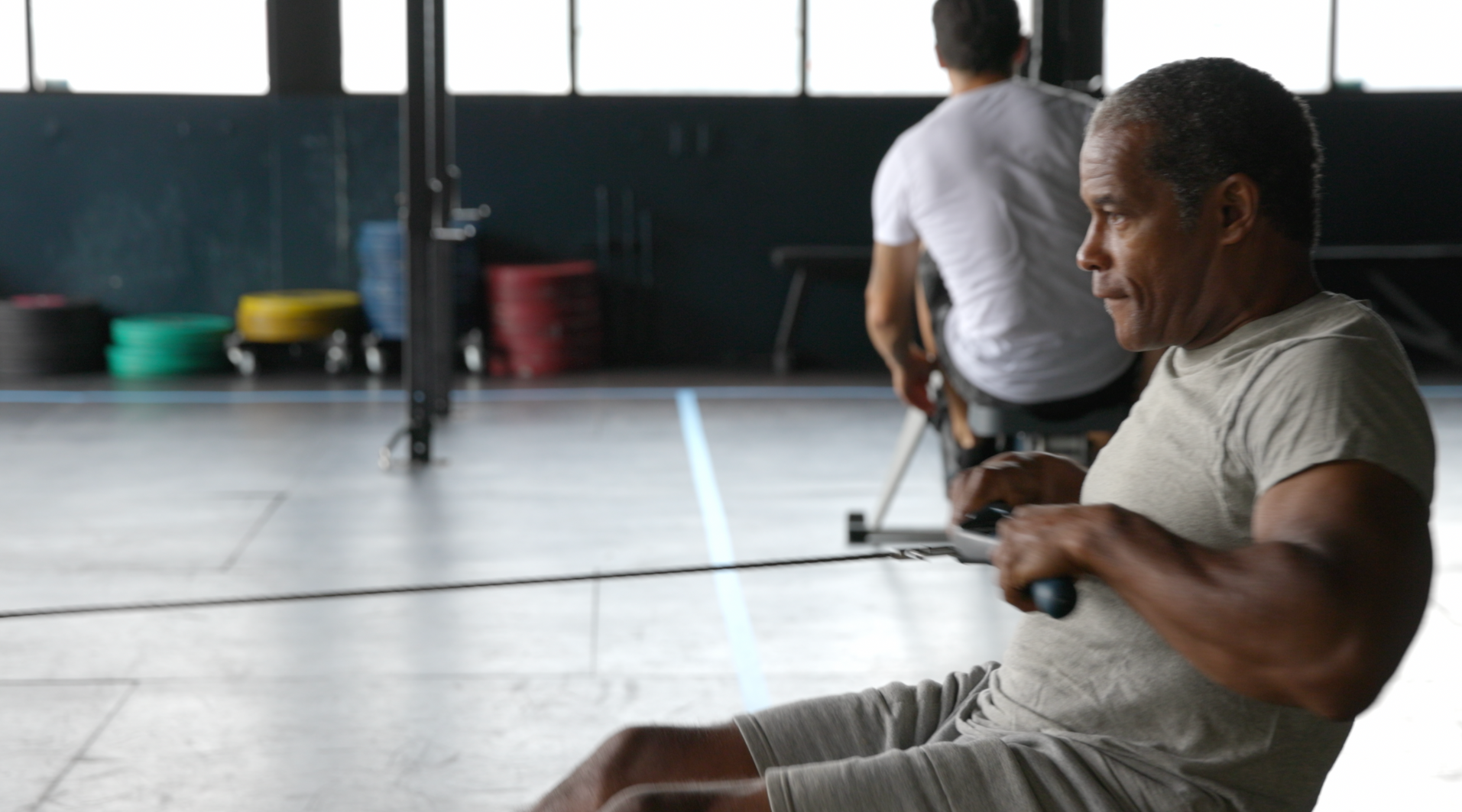 Two men on rowing machines at gyms with yoga classes