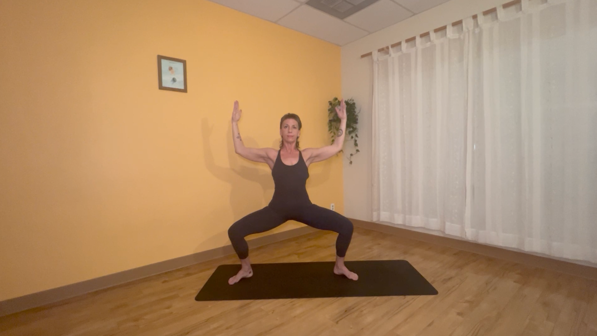 yoga teacher standing on mat practicing moon salutations in goddess pose