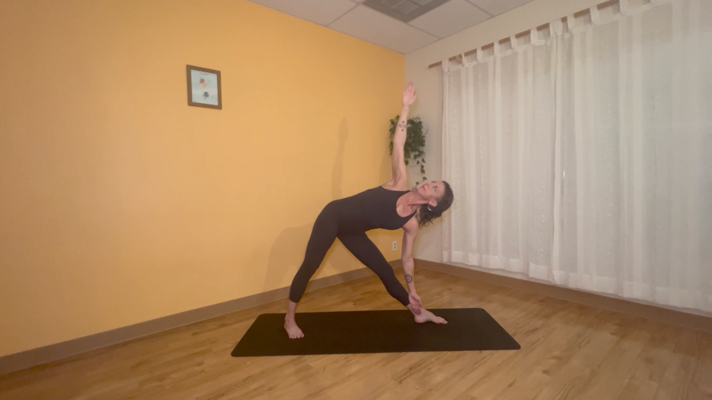yoga teacher standing on mat practicing moon salutations in triangle pose