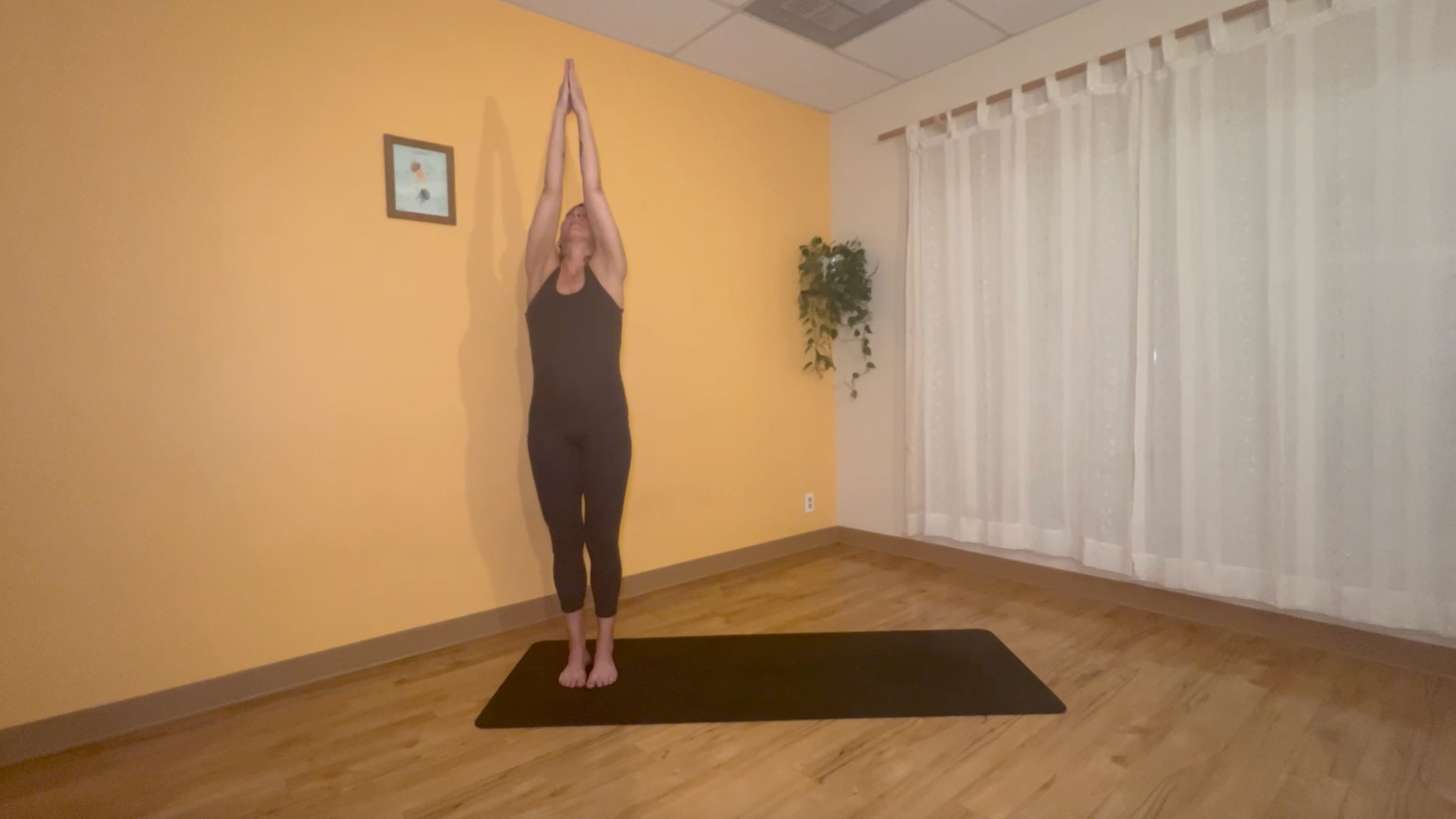 yoga teacher standing on mat practicing moon salutations in upward salute