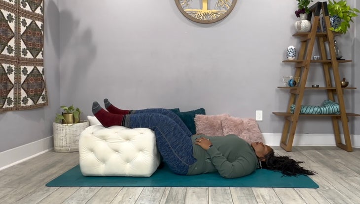A yoga teacher in a Restorative Yoga pose with calves propped on top of an ottoman.
