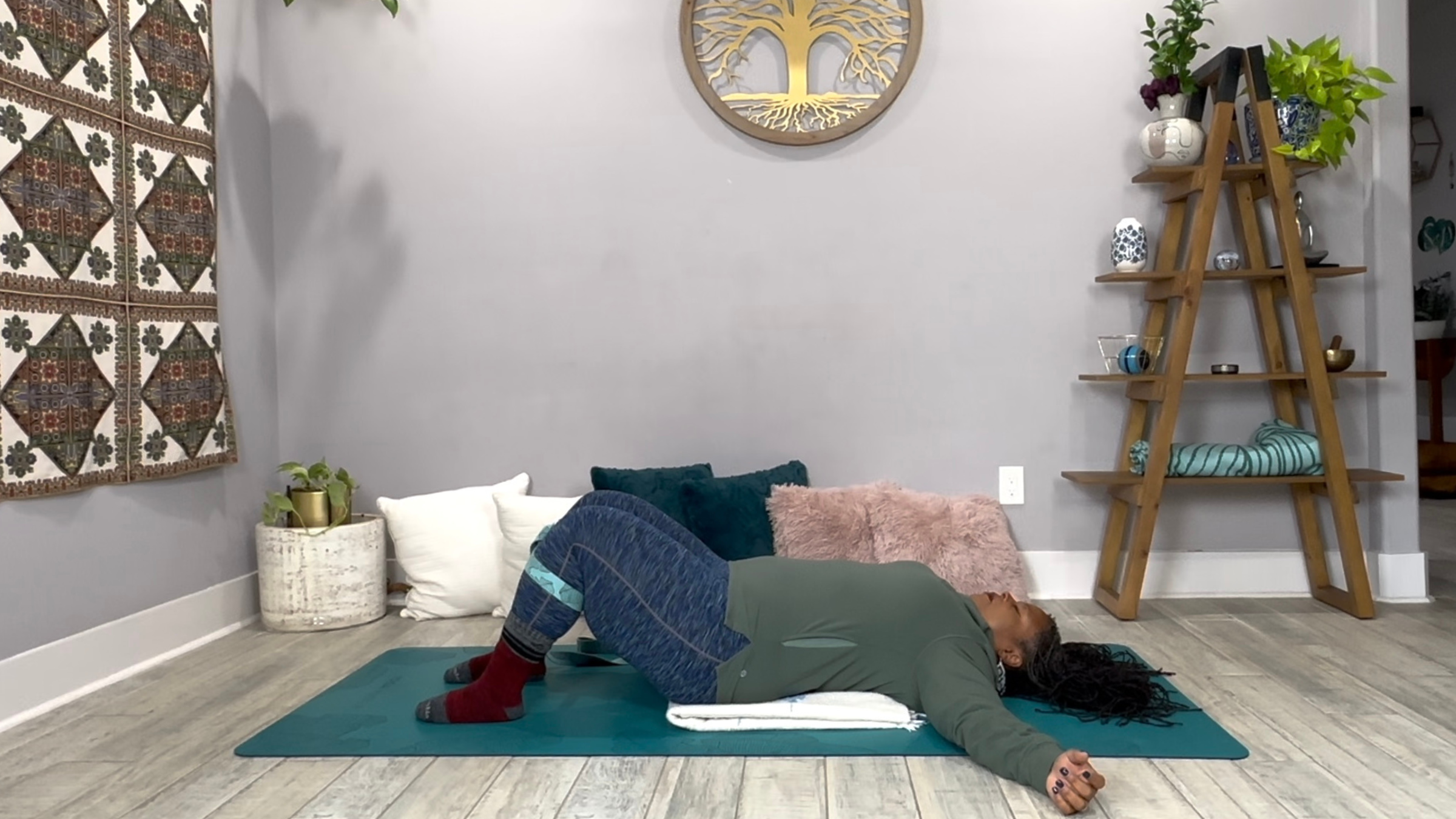 A yoga teacher on her back in a Restorative Yoga pose with a folded blanket beneath her back.