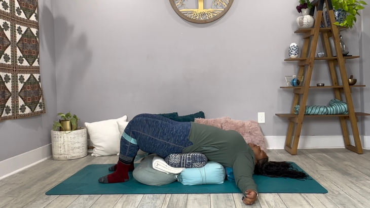 A yoga teacher in a Restorative Yoga pose, laying over a pile of pillows and bolsters.