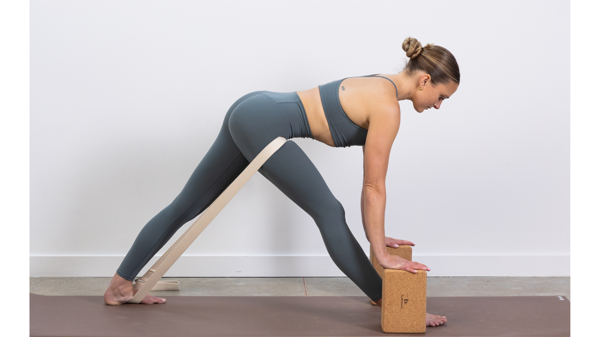 Yoga teacher with block beneath hands and a strap around back leg in Pyramid Pose