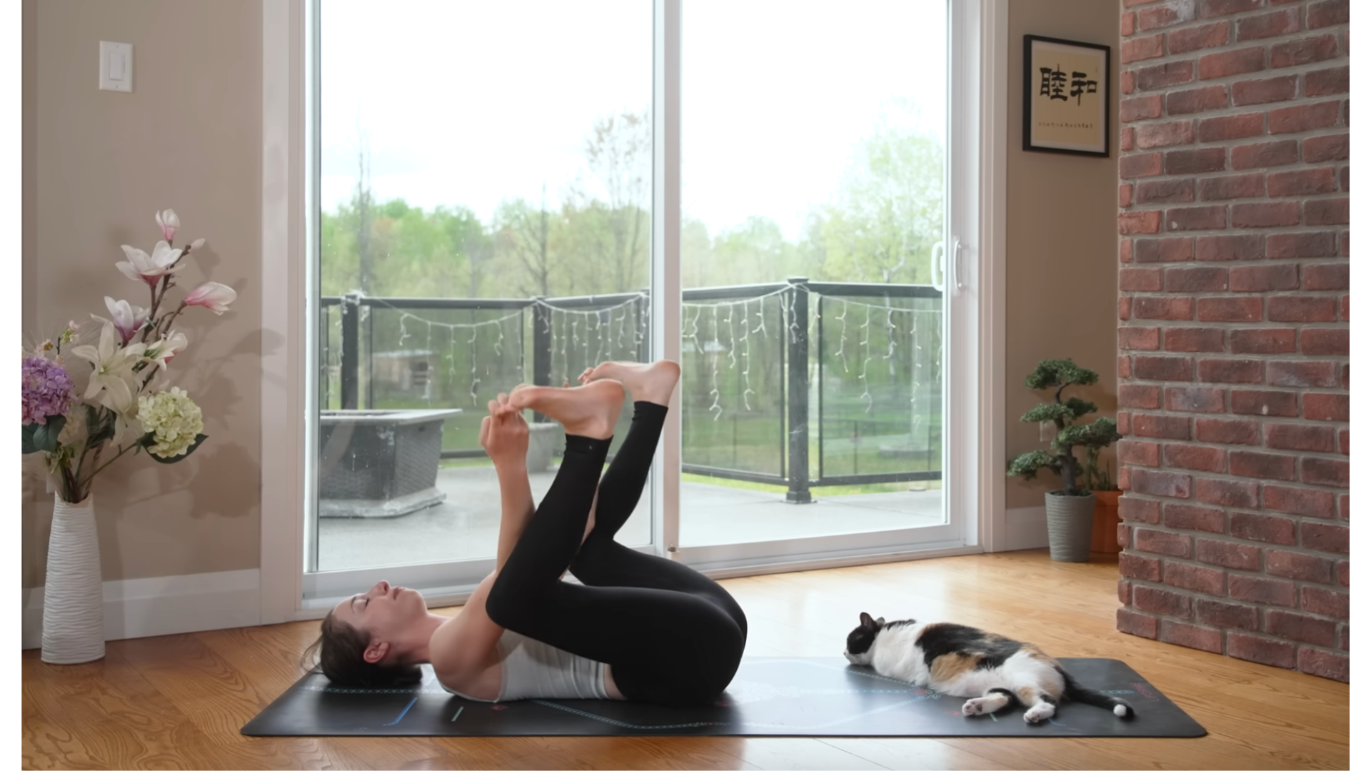 Yoga teacher lying on her back on a mat grabbing her toes in Happy Baby Pose