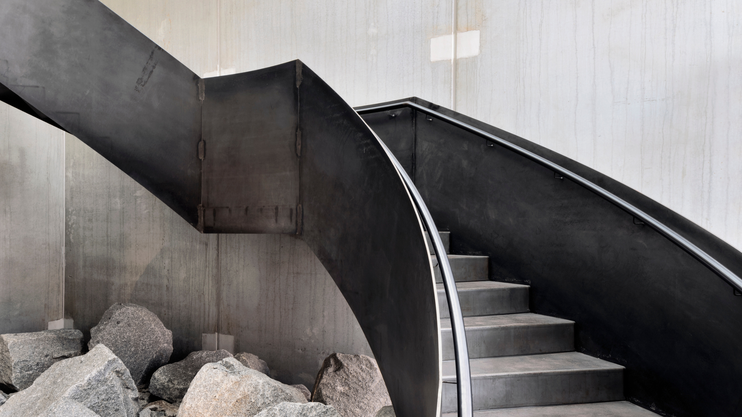 Metal and concrete open modern staircase above boulders