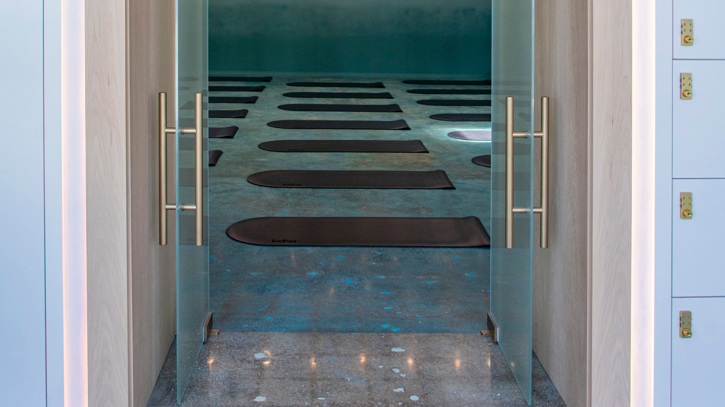 Looking through a double glass door frame into a teal-colored room with yoga mats laid out on the floor
