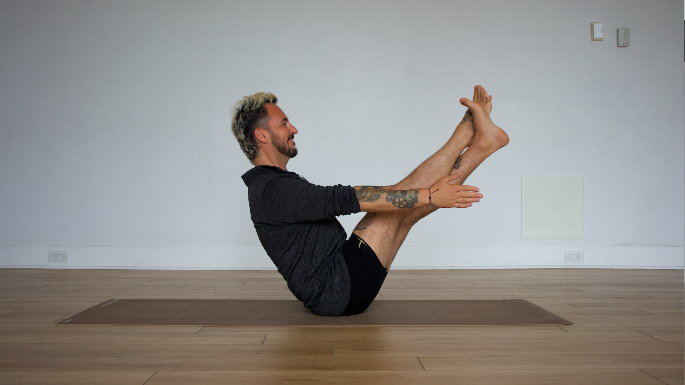 Man in modified boat pose with leg wrap on yoga mat