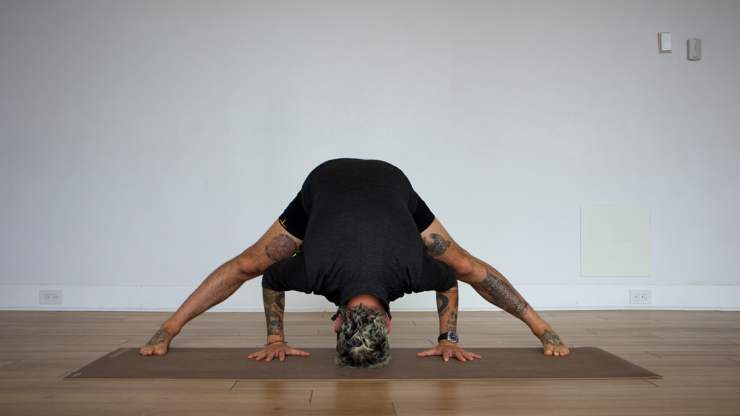 man in wide-legged forward fold pose on yoga mat