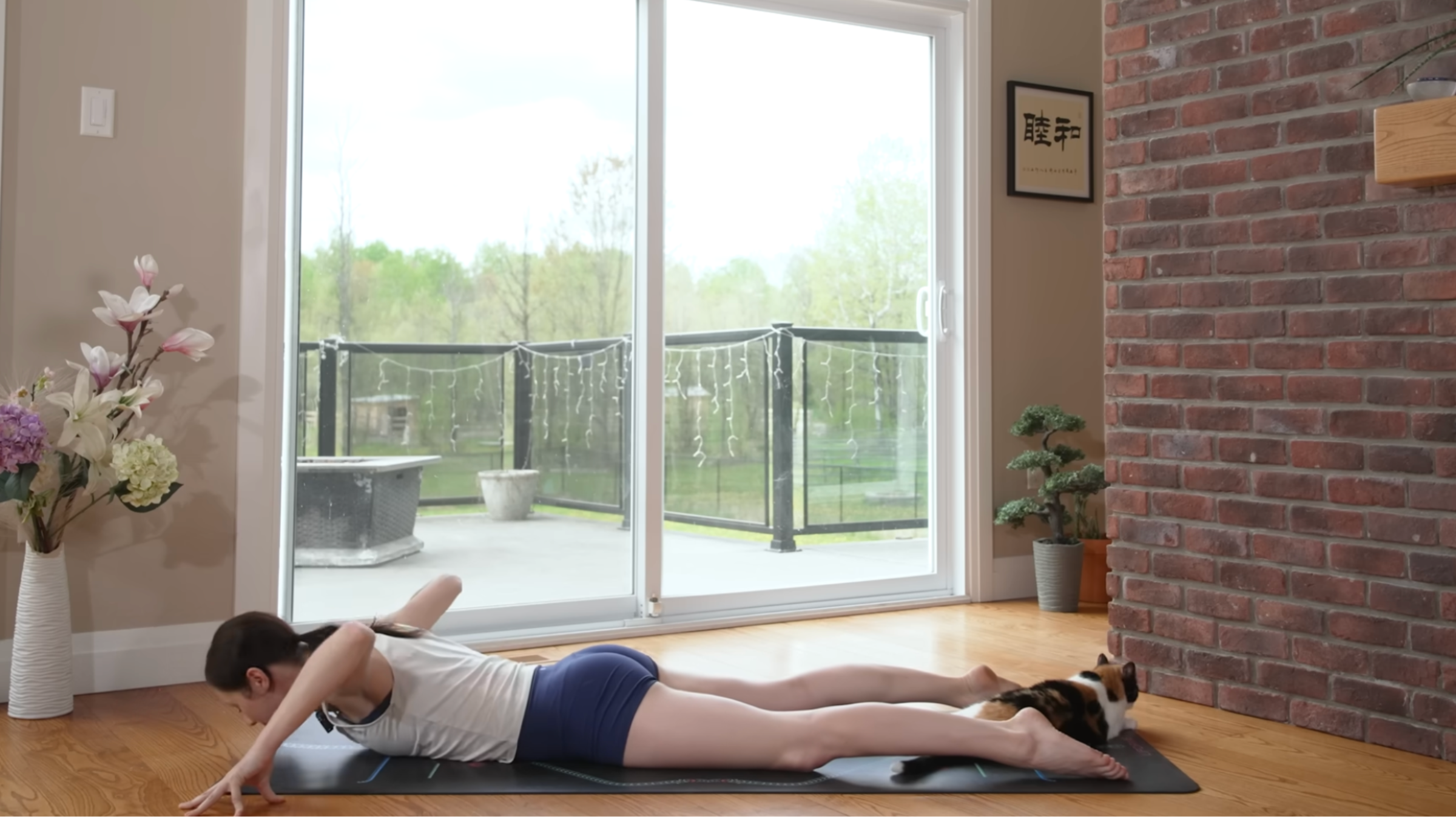 woman preparing to push up to cobra pose on yoga mat in home with cat between feet