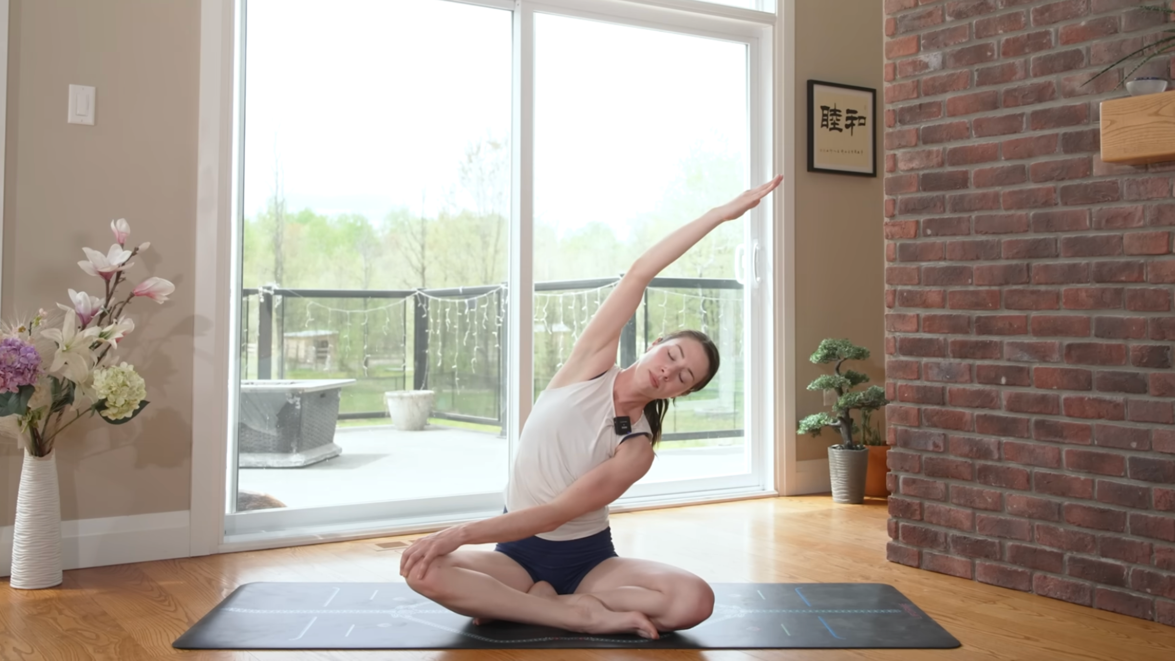 woman does seated stretch with right arm overhead on yoga mat in home