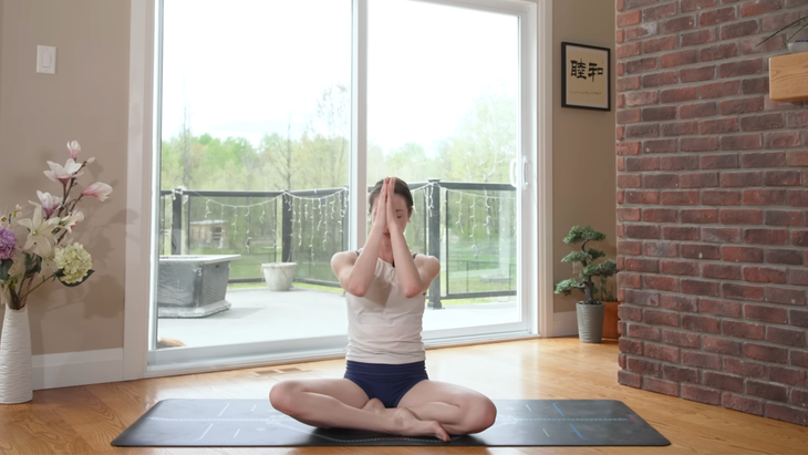 woman in seated meditation on yoga mat with hands to forehead