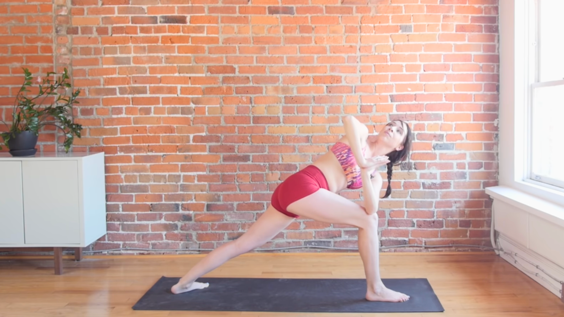 woman in revolved warrior 1 pose with right foot forward and left elbow on outside of right knee and face toward the ceiling