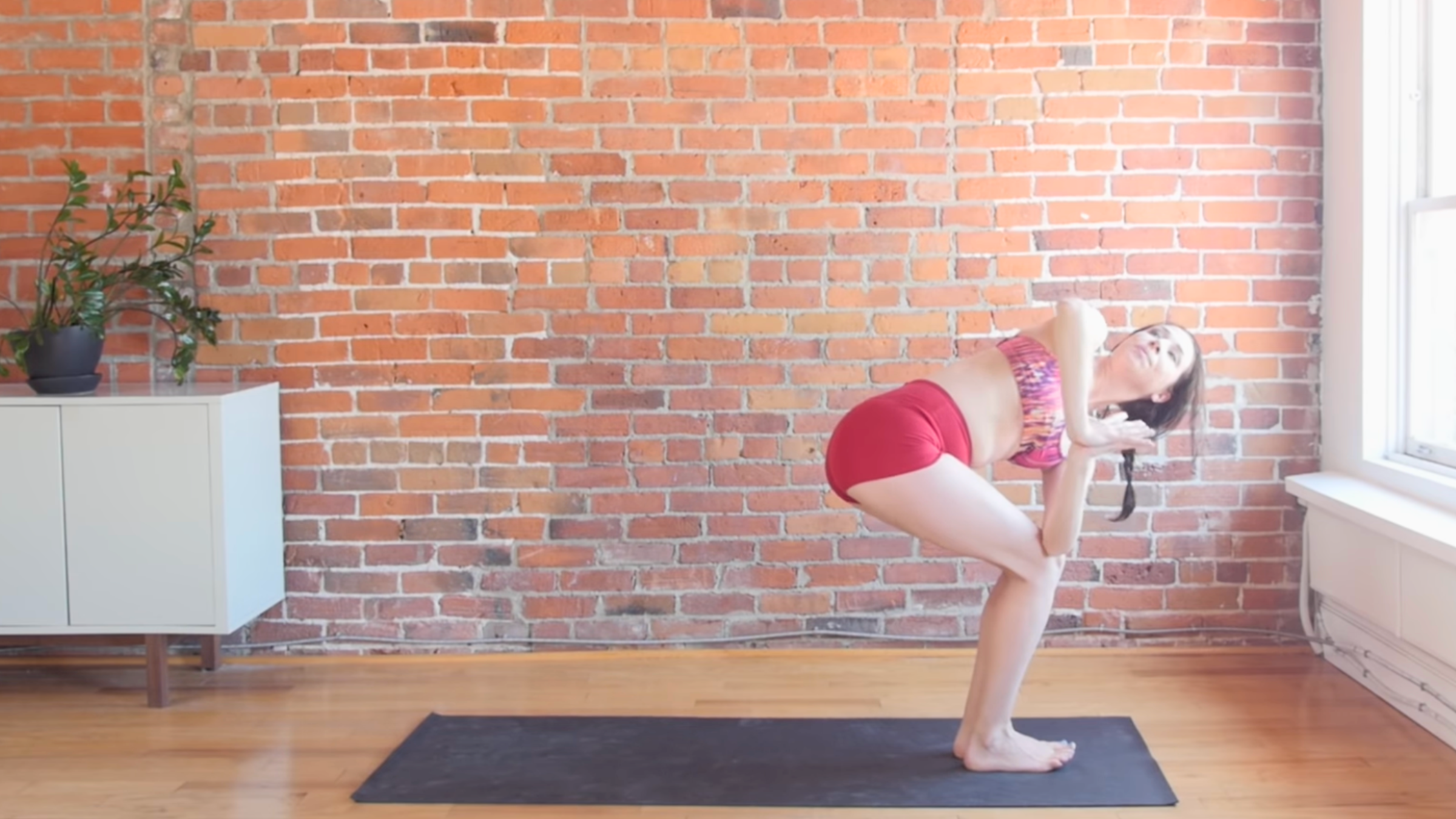 woman in revolved chair pose with legs in chair and left elbow outside of right knee and face toward ceiling