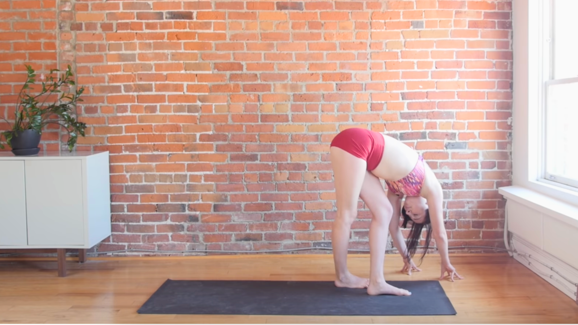 woman doing standing IT band stretch with legs crossed and feet on ground on black yoga mat