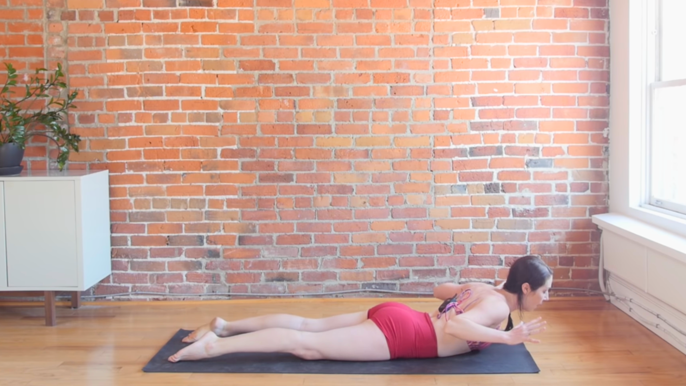 woman in cobra pose with hands lifted off the ground on top of black yoga mat in front of brick wall