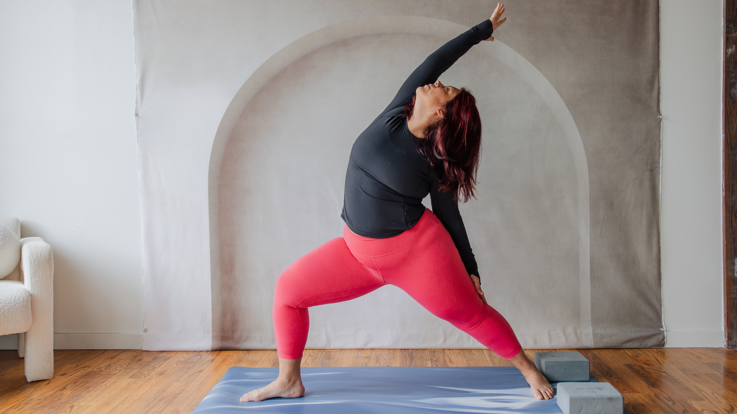 woman in black shirt and red yoga pants in reverse warrior with right leg forward and left hand on back of left thigh with right arm extended overhead and face toward ceiling