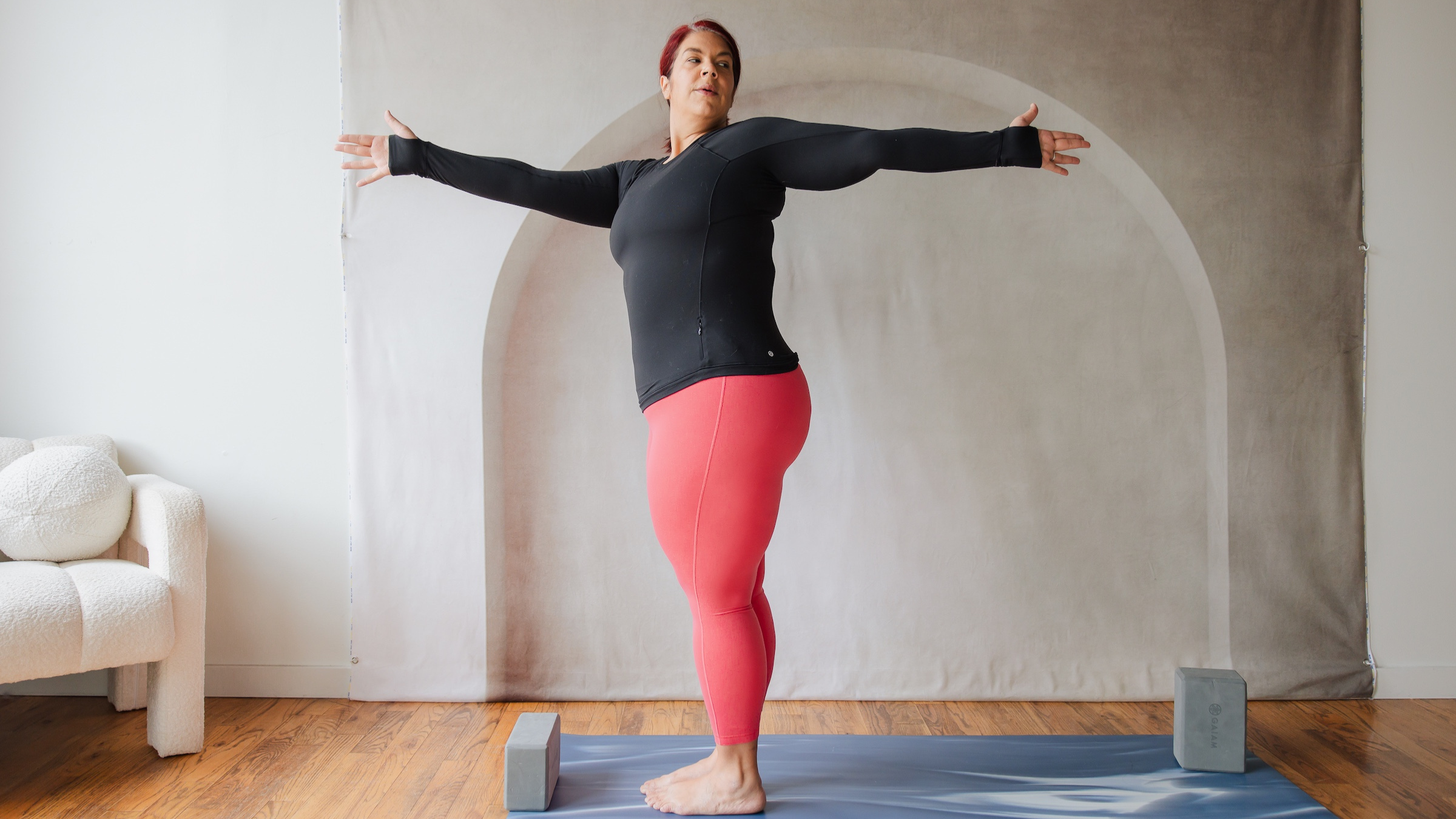 woman in black shirt and red yoga pants stands in sun salutation with her arms out and upper body twisted