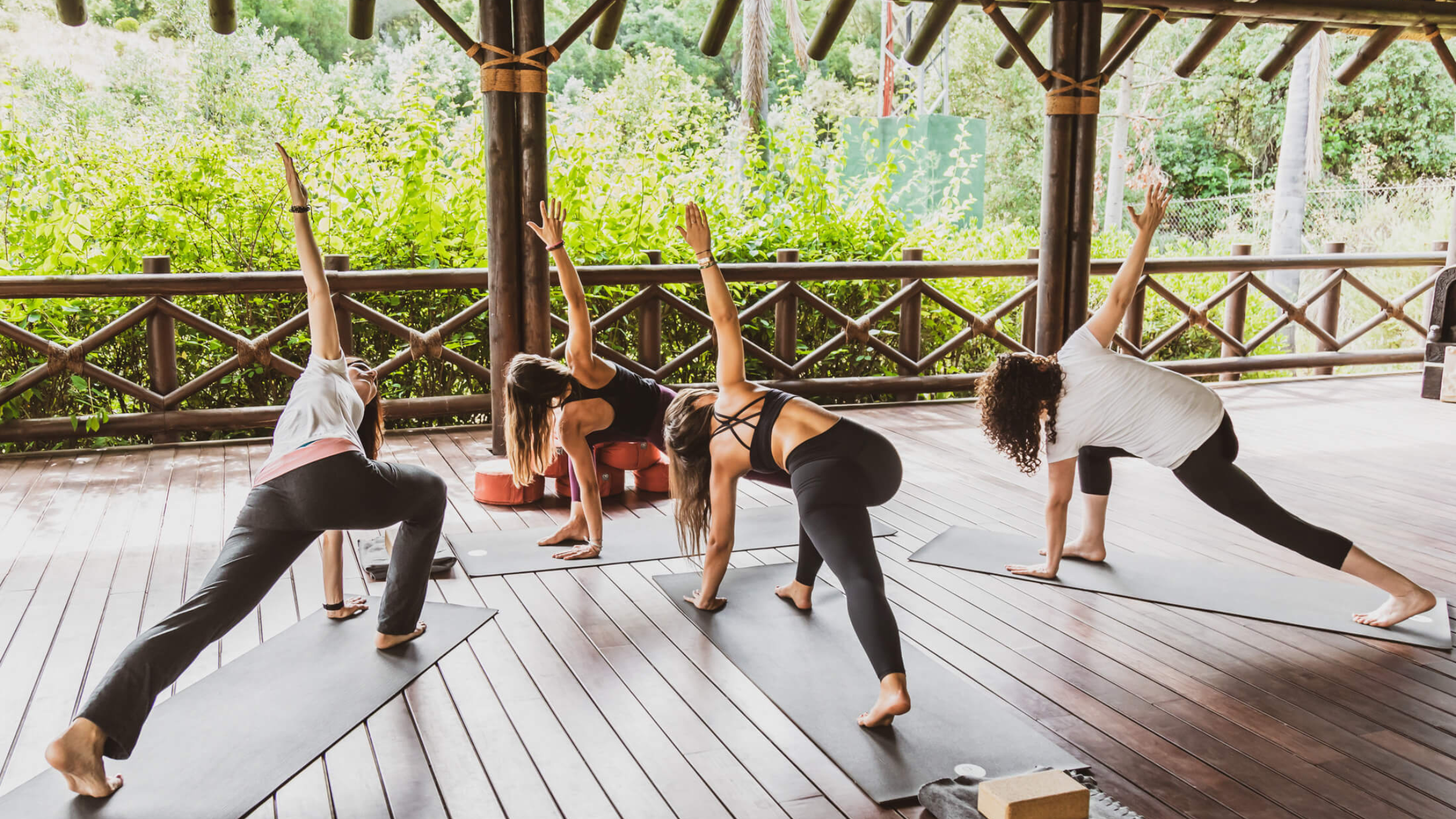 four women practice yoga on a wooded deck in front of trees