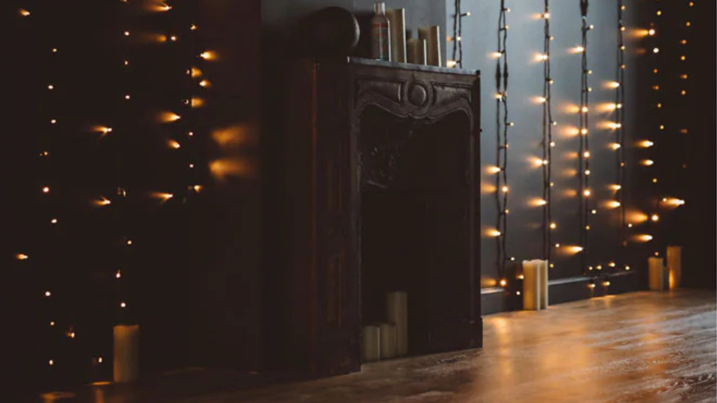 black mantel with twinkly lights and candles along wall next to it.