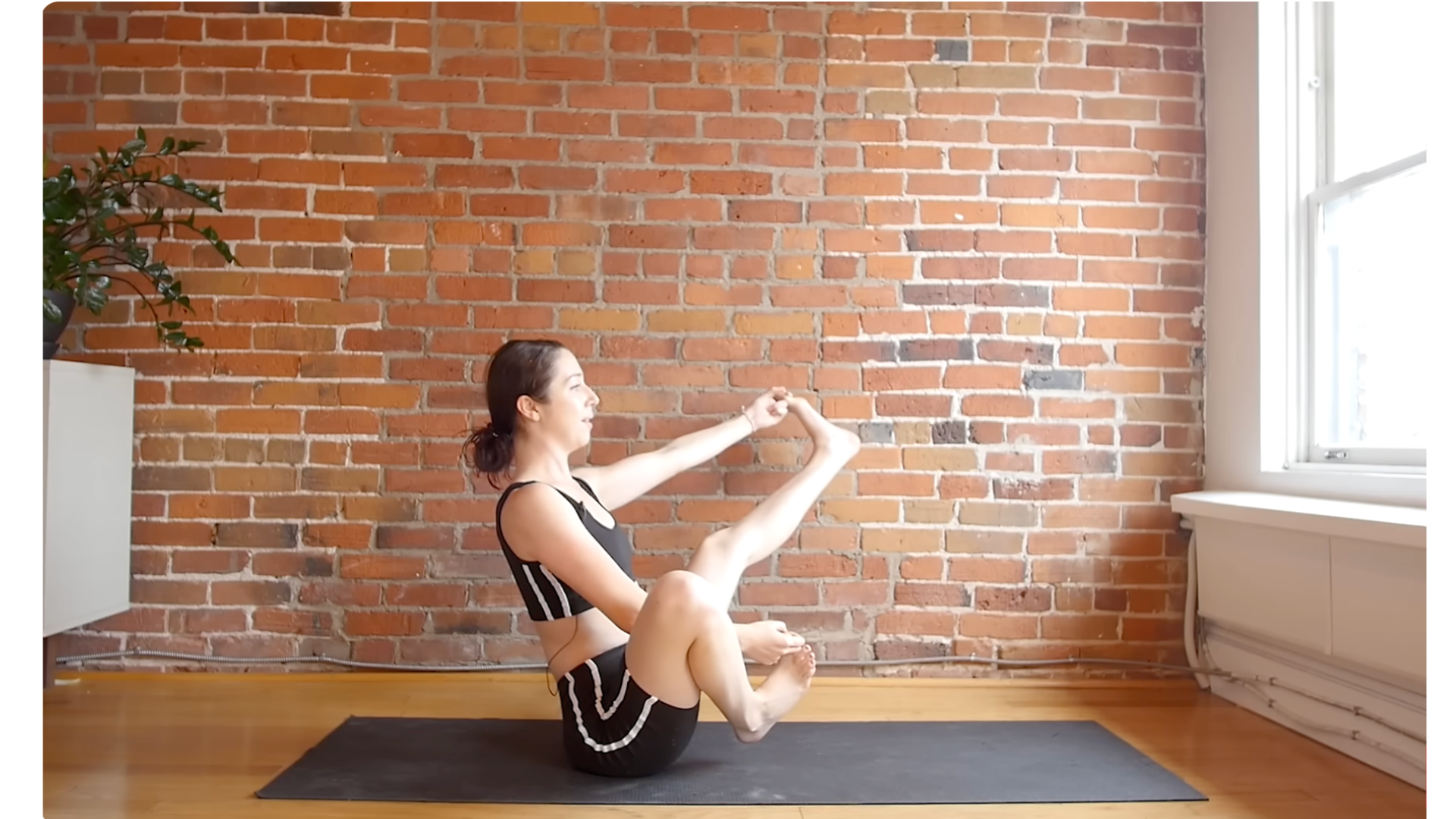 Yoga teacher leaning back on her yoga mat with one leg extended straight and the other bent in a balancing pose