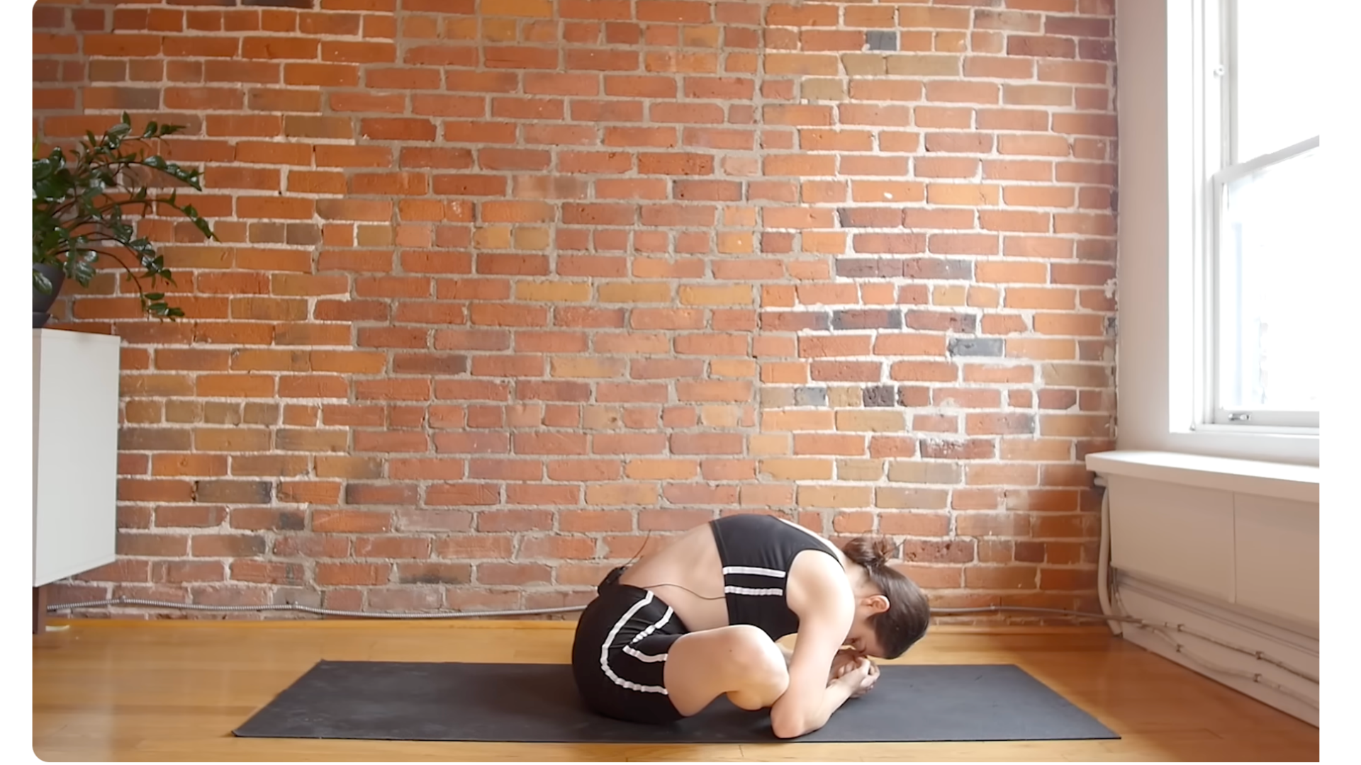 Yoga teacher sitting on a mat with her knees bent and her feet drawn toward her hips as she leans forward in a full-body stretch