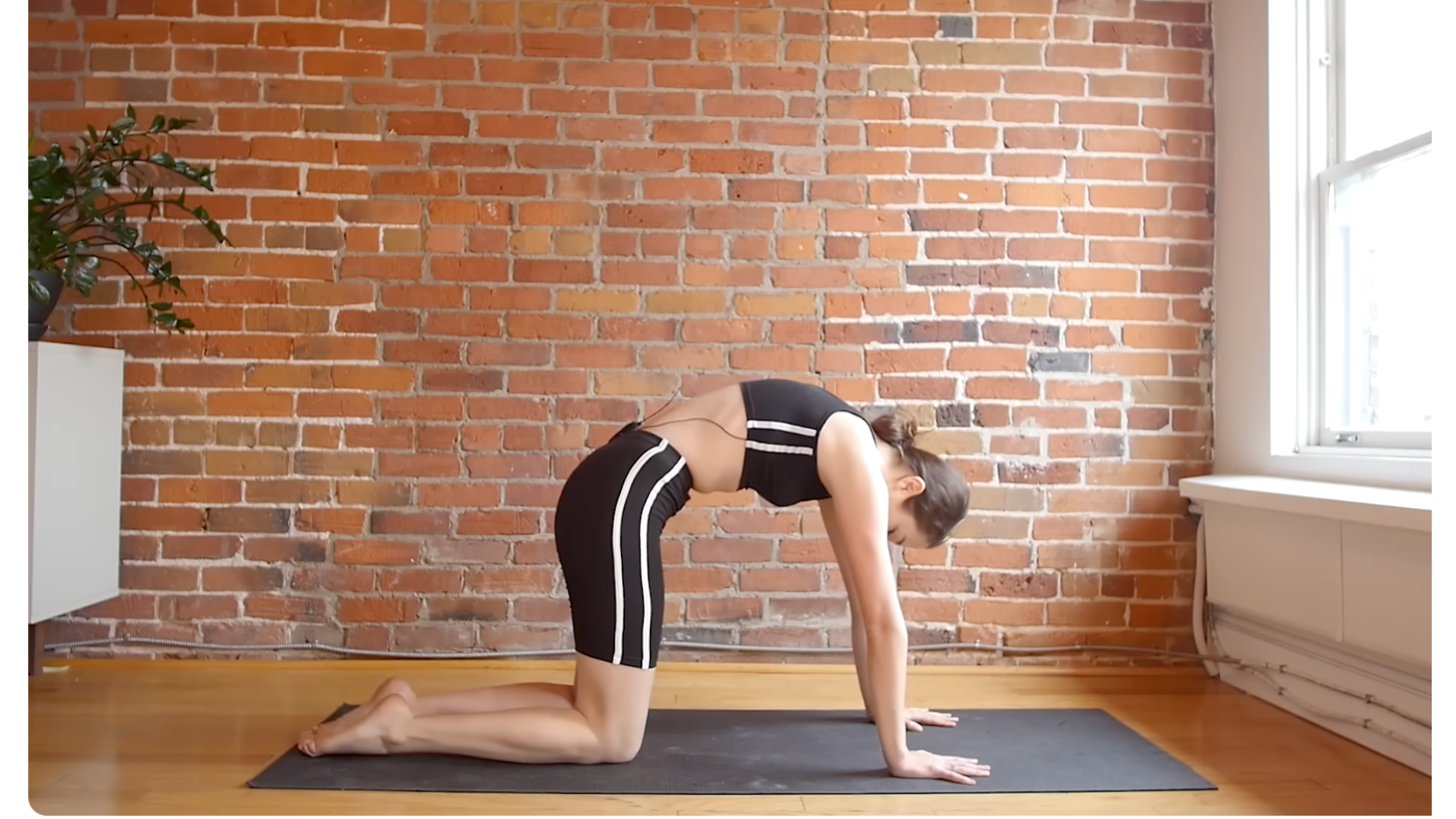 Yoga teacher kneeling on a mat with her back rounded in Cat Pose