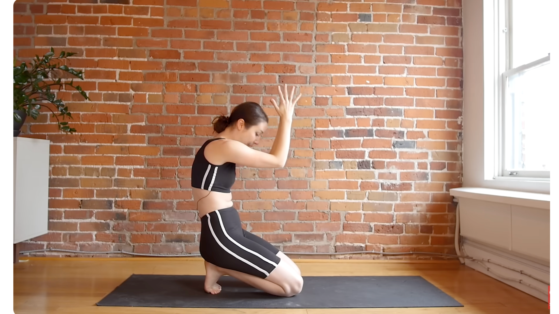 Yoga teacher kneeling on a mat while leaning back on her heels and sitting up while rounding her back in a version of Cat Pose