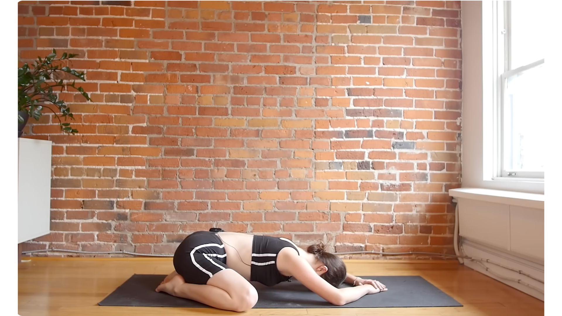 Yoga teacher practicing Child's Pose on a mat during a 10-minute morning yoga full-body stretch session